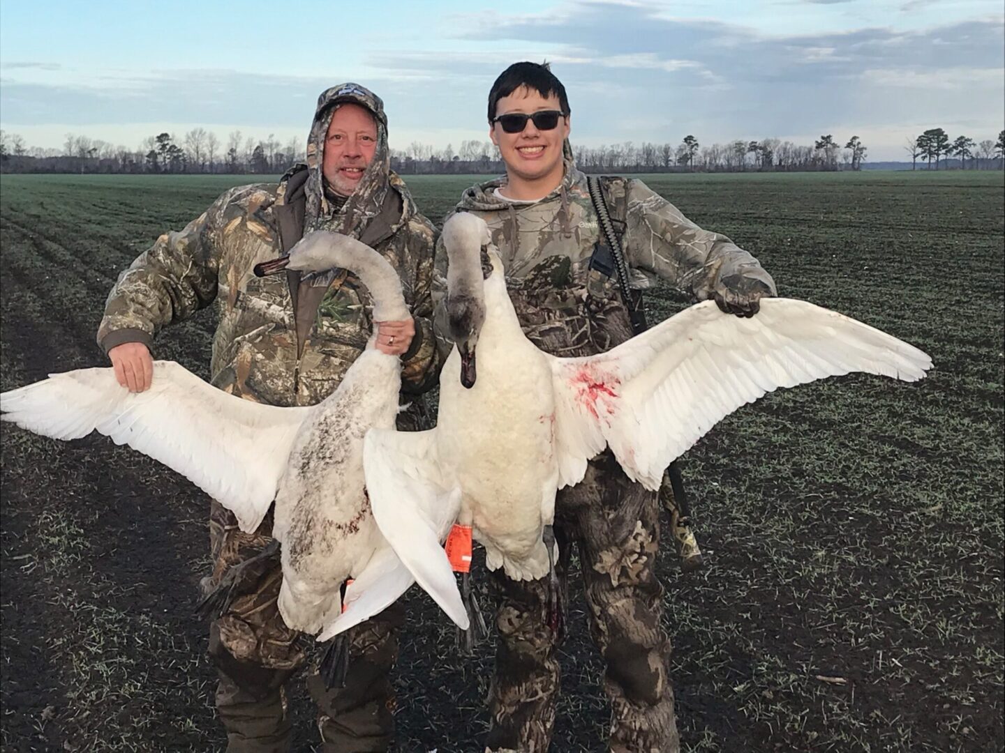 Two men holding a goose and another duck.